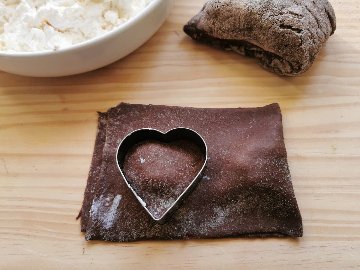 A sheet of chocolate pasta dough folded over the filling with a heart-shaped cookie cutter on top.
