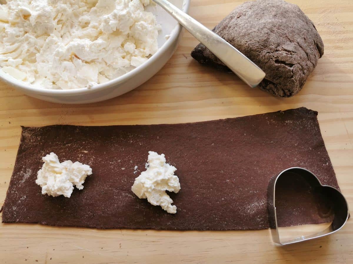 A sheet of chocolate pasta dough with teaspoons of ricotta and mascarpone filling on one side.