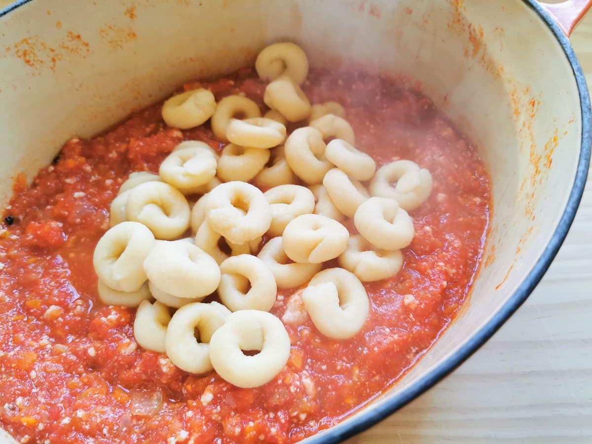 cooked homemade pasta rings in Dutch oven with tomato and ricotta sauce