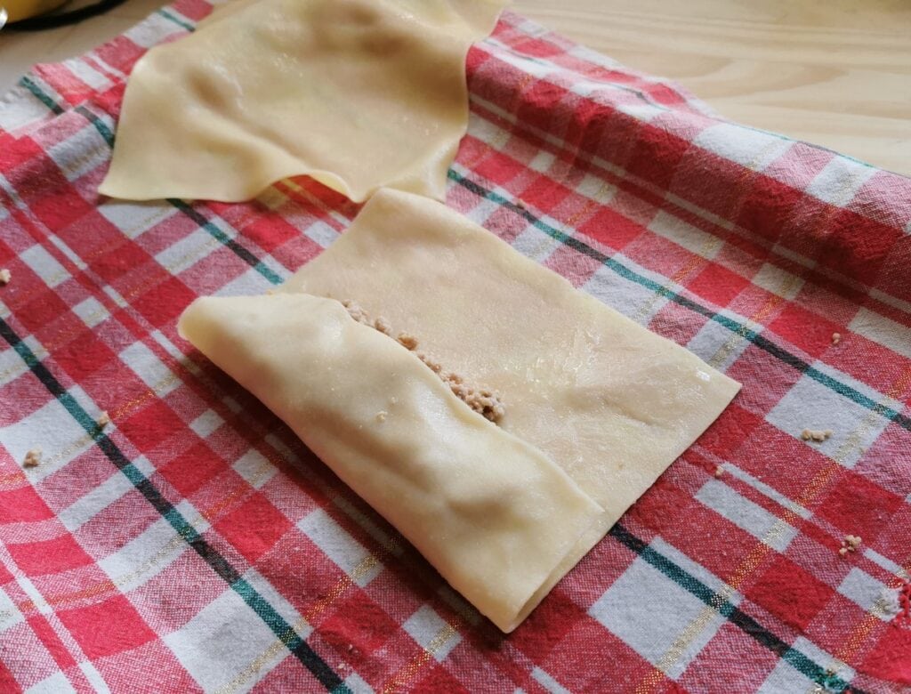 parboiled pasta sheet being rolled around cannelloni filling.