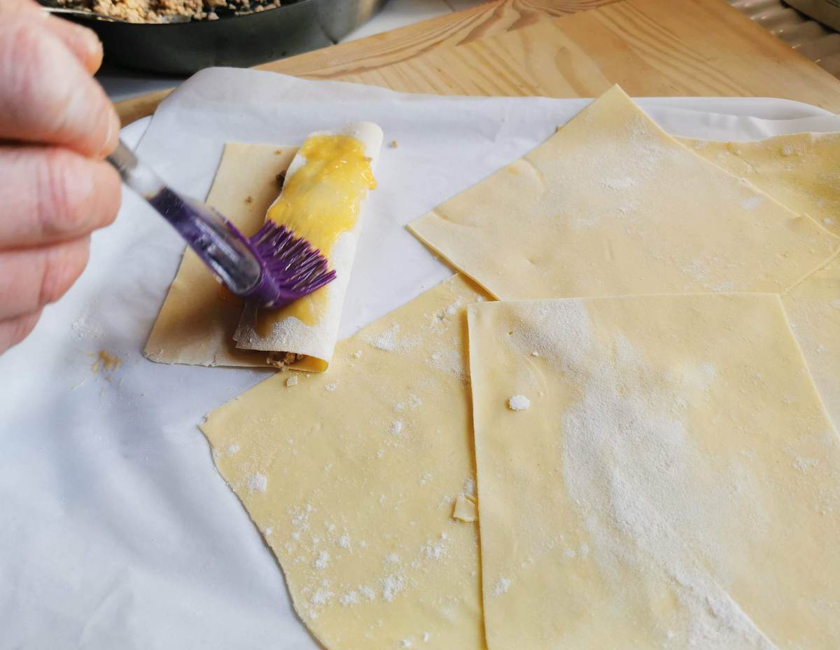 fresh pasta sheet being rolled around filling and brushed with egg yolk