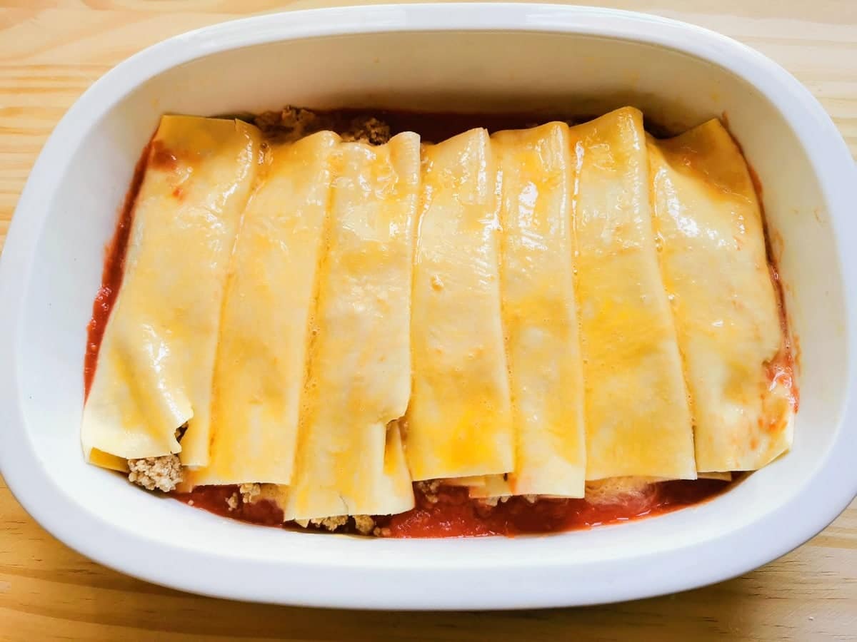 uncooked homemade cannelloni in oven dish on top of tomato sauce.