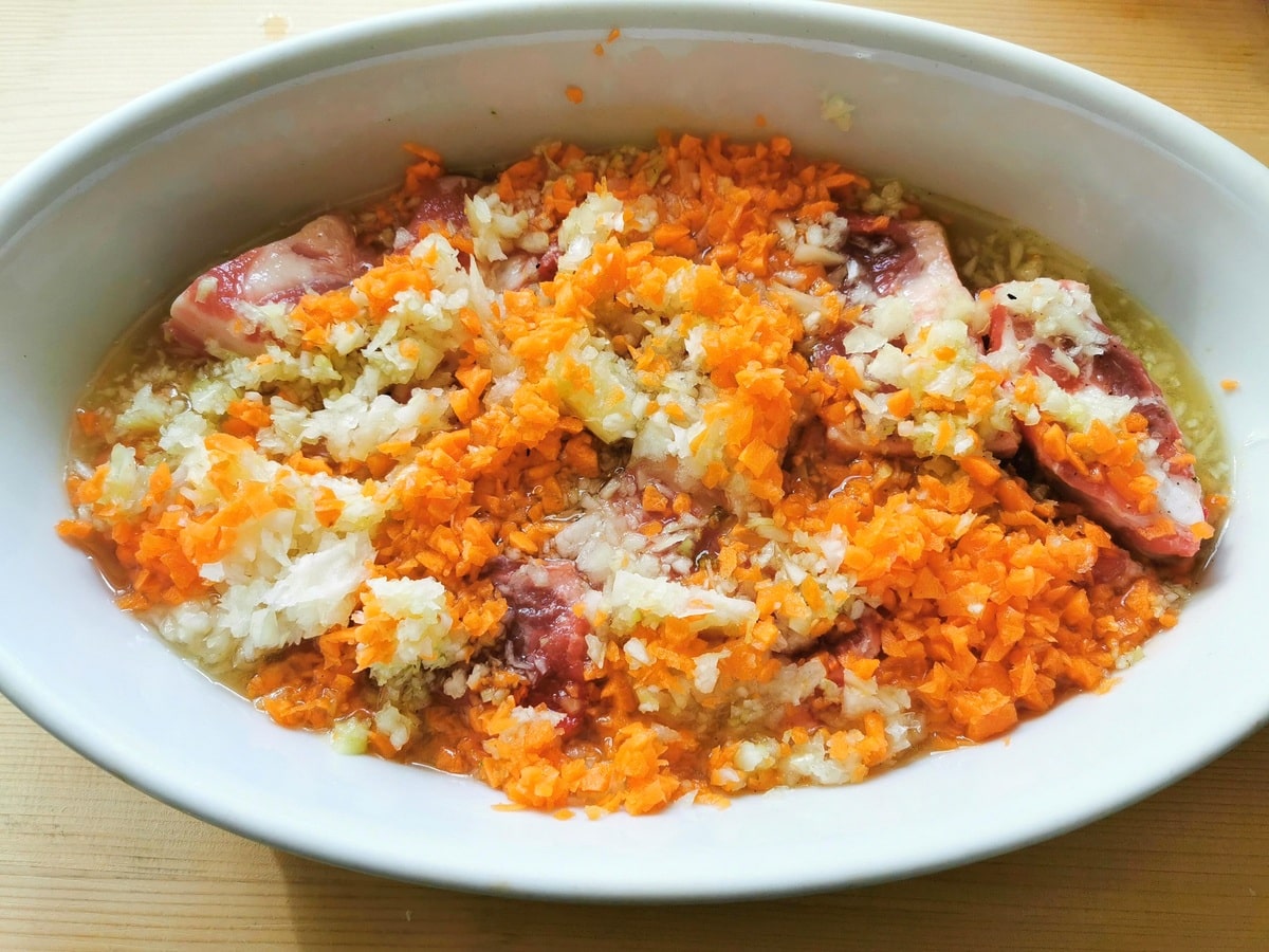 chopped carrots, onions and celery with pork ribs and vegetable stock in oven dish