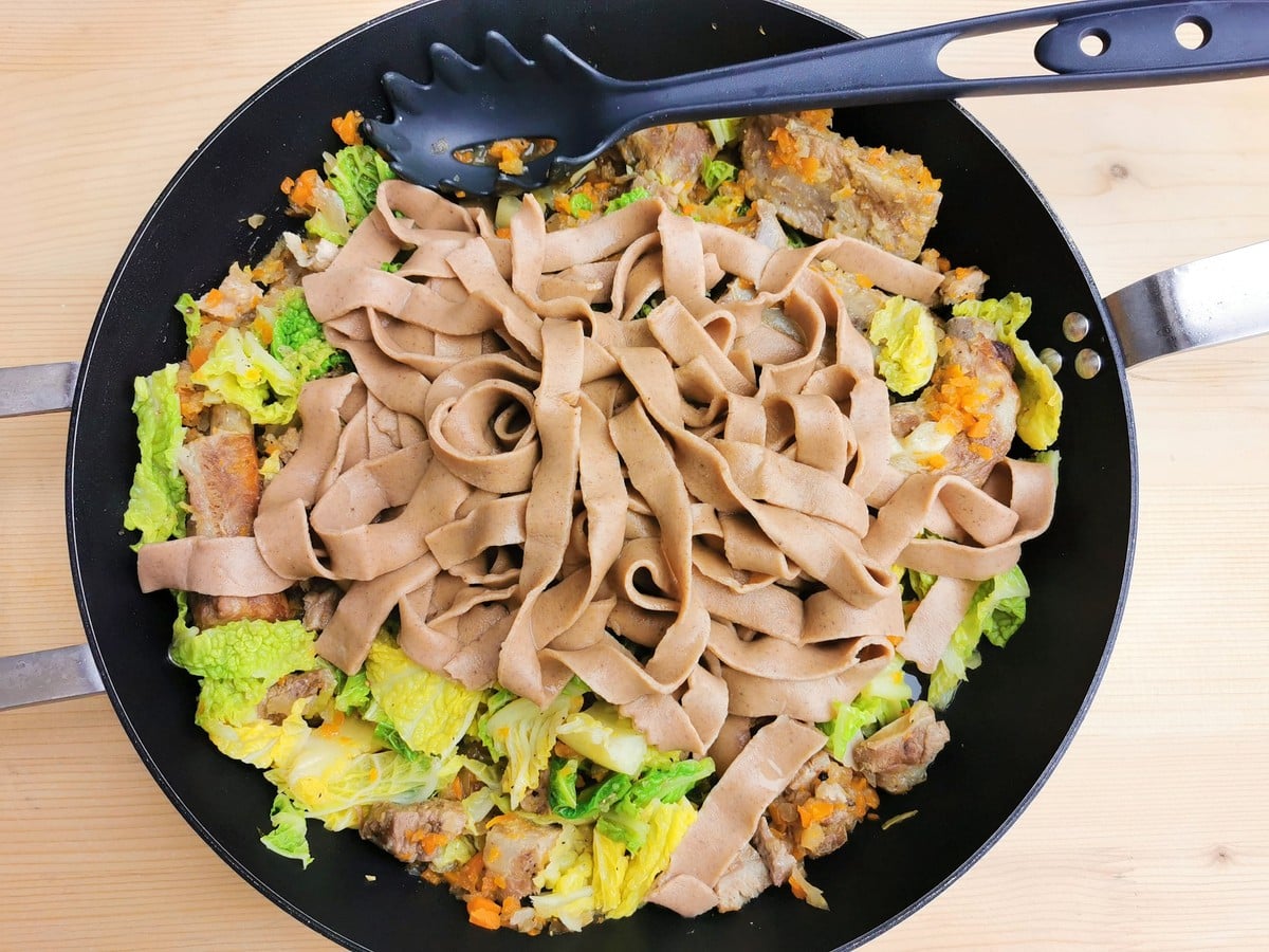 cooked homemade chestnut pasta with pork and cabbage sauce in pan