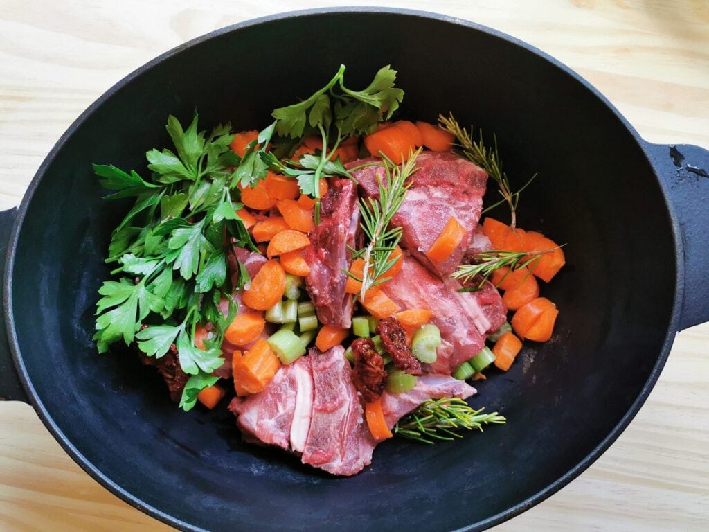 lamb neck bones with vegetables and herbs in Dutch oven