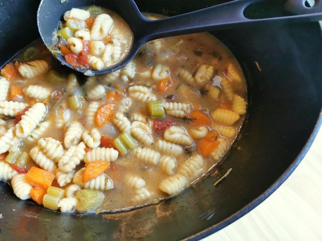 homemade Sardinian gnocchi cooking in broth in Dutch oven.