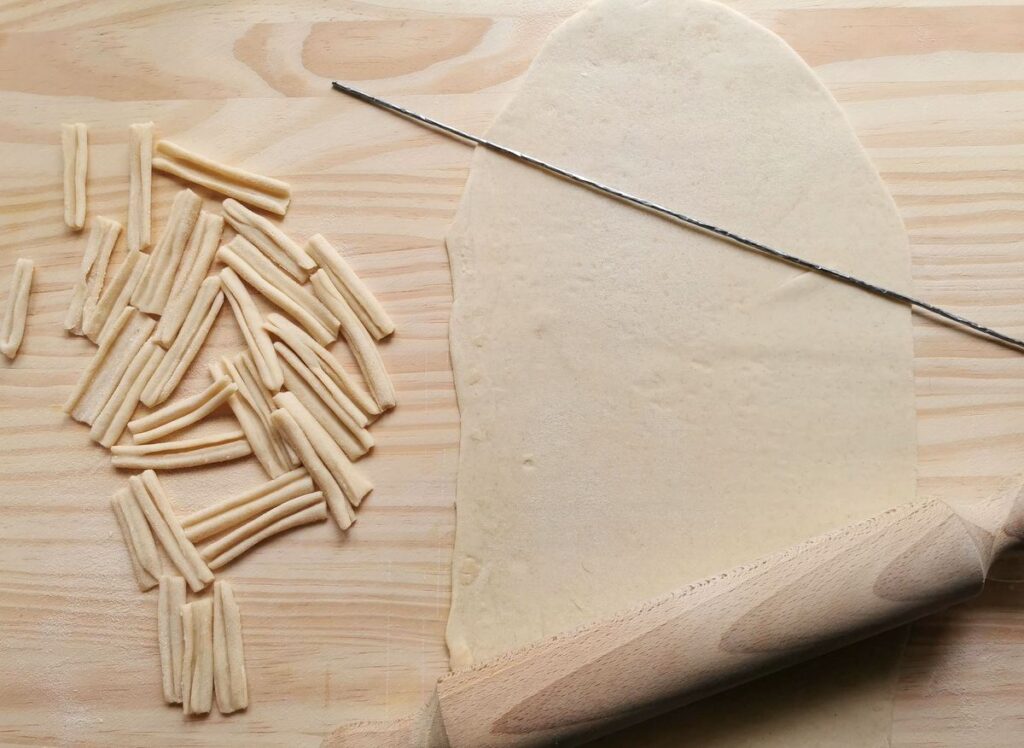 rolled out sheet of pasta dough with some ready cassarecce, a rolling pin and a 'ferro'.