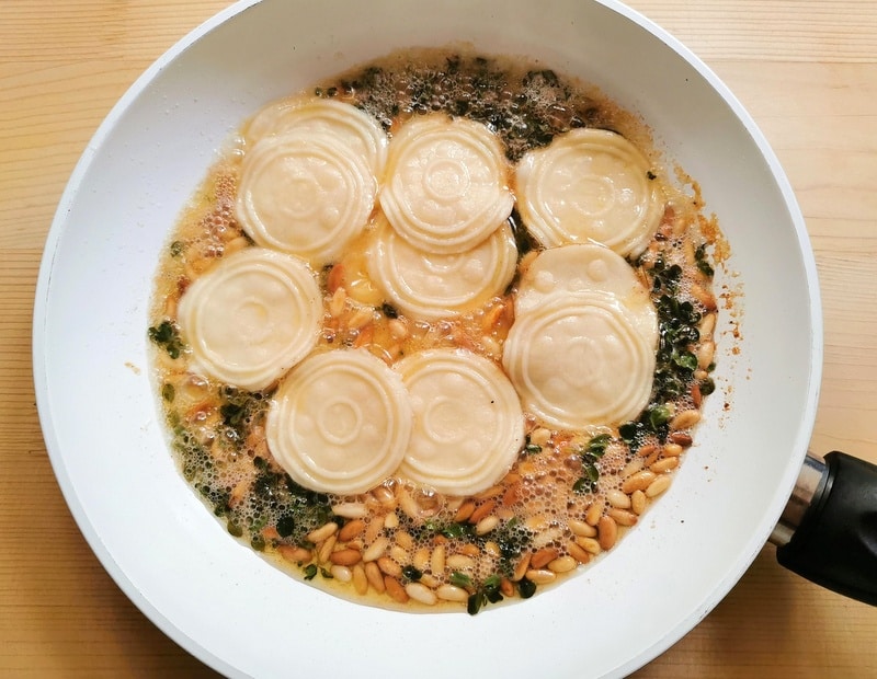 cooked homemade corzetti in pan with melted butter, pine nuts and marjoram