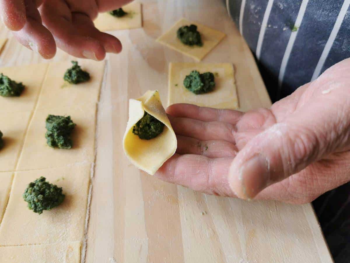 Man making fagottini pasta by first joining two opposite corners of a pasta square together to form a triangle.