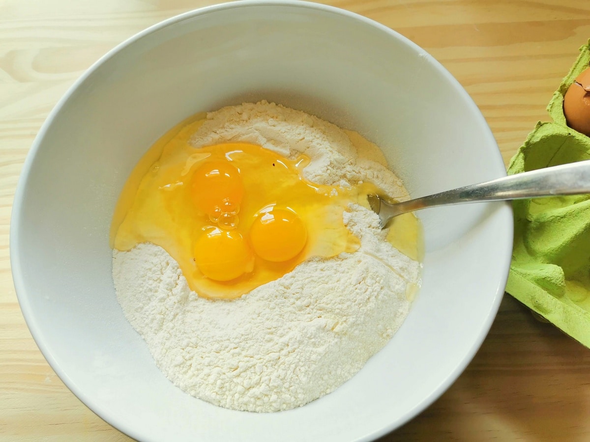 Two types of flour and eggs in a white bowl.