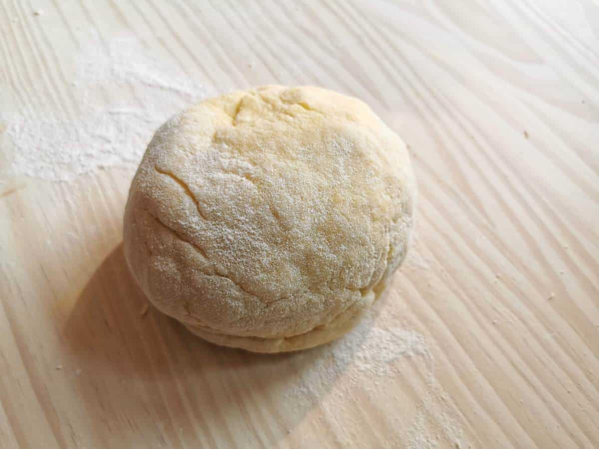 Ball of kneaded pasta dough on wood surface.