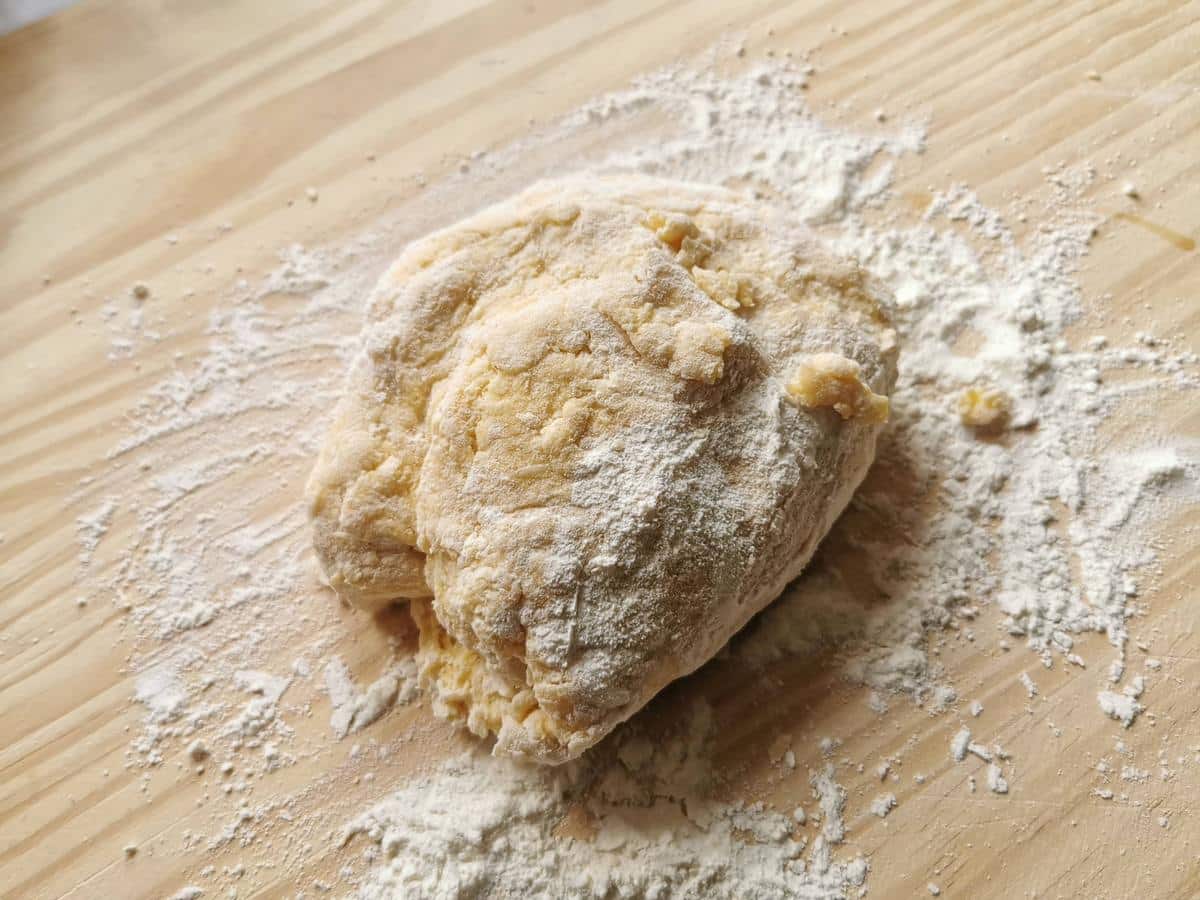 Ball of unkneaded pasta dough on flour dusted wood surface.
