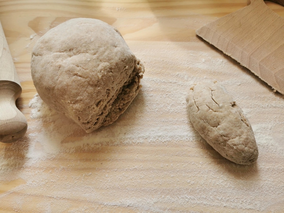 Piece of rye flour ravioli dough cut off from larger dough ball on wood worktop.