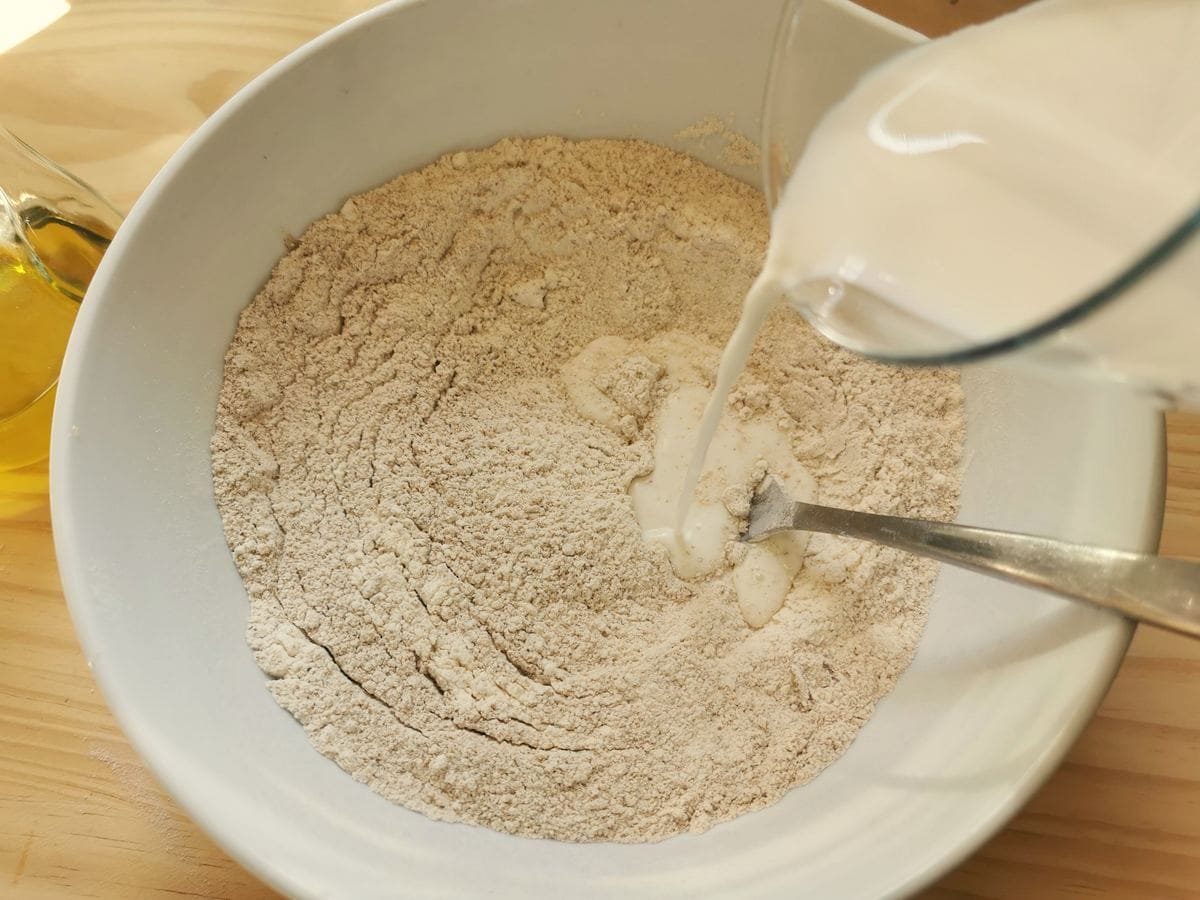 Milk being poured into white bowl with flour.