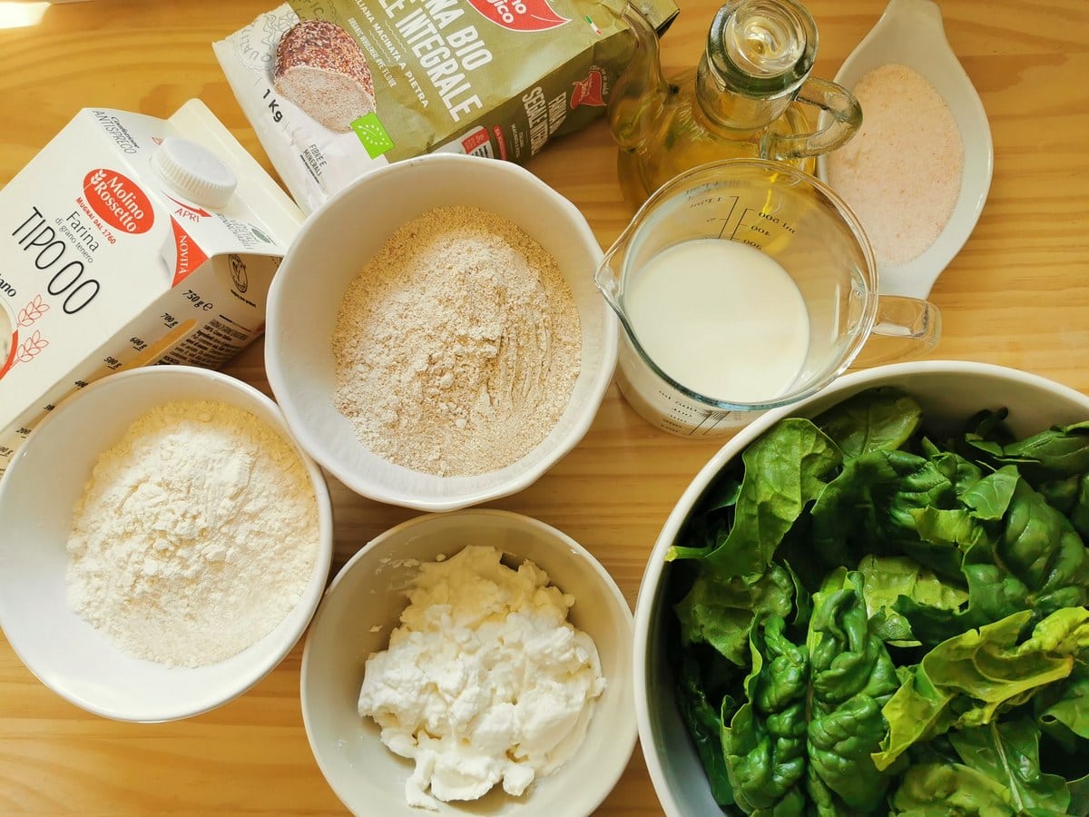 Ingredients for rye flour ravioli filled with ricotta and spinach on wood pastry board.