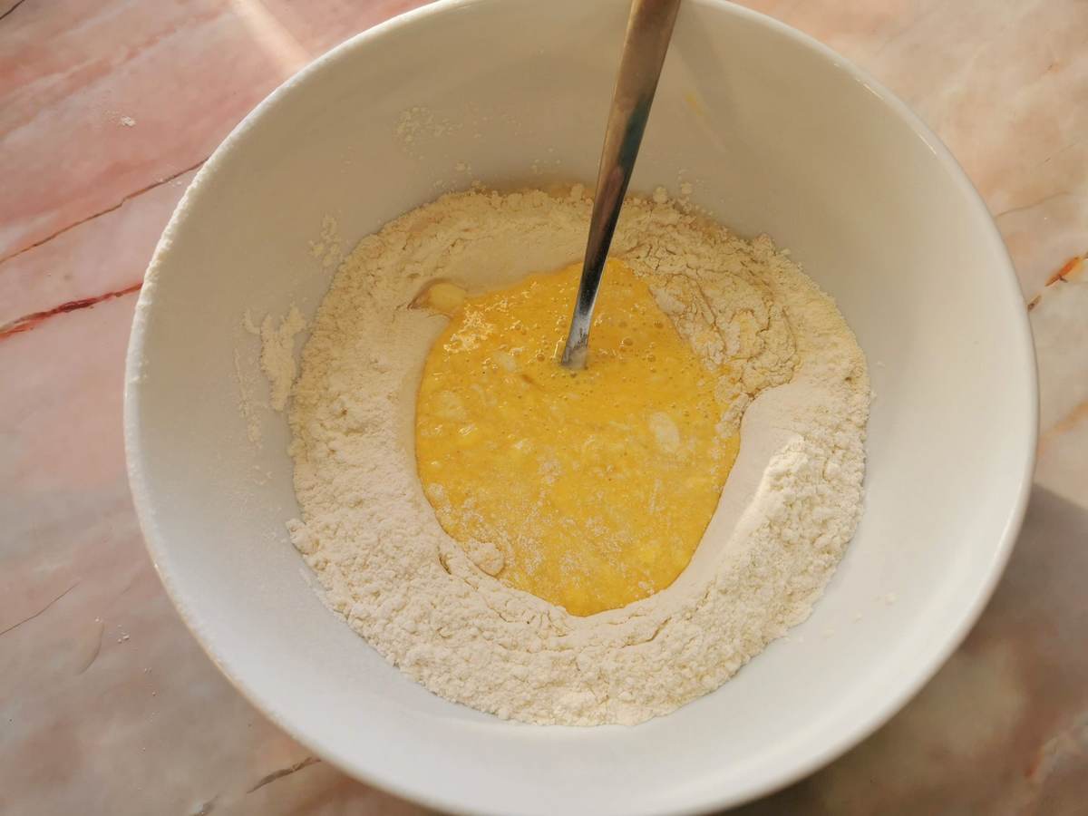 Beaten eggs in the middle of flour in a bowl.