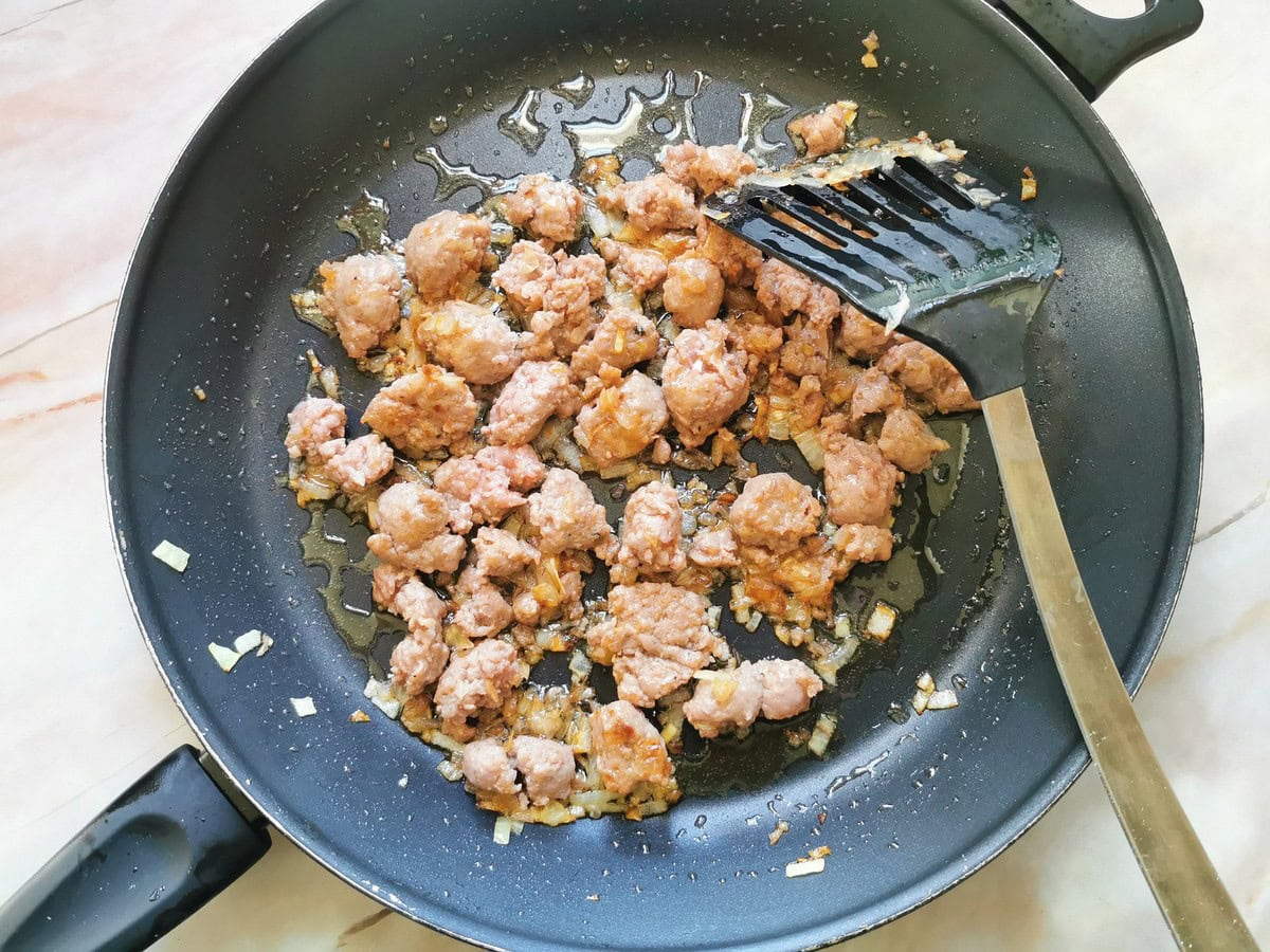 Browned sausage pieces in skillet with onions.