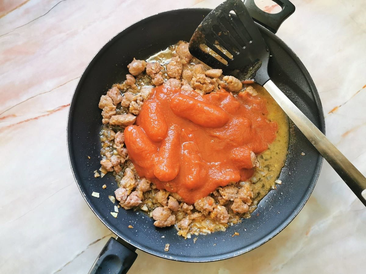 Canned peeled tomatoes added to sausage pieces in skillet.