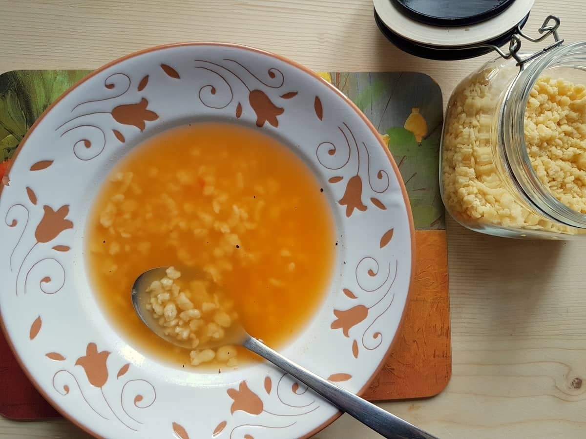 Homemade grattini in broth in white bowl with spoon.