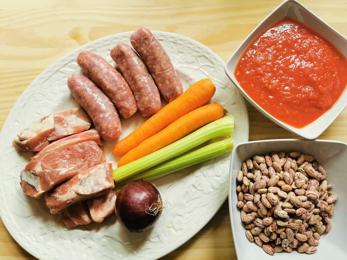 vegetable and meat ingredients for sausage and bean sauce on white plate. Borlotti beans in white bowl and tomato passata in white bowl.