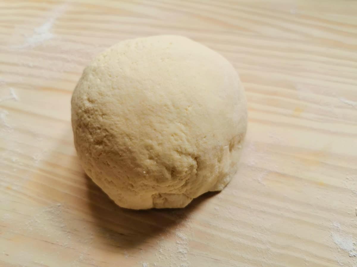 ball of maltagliati dough on wooden pastry board.