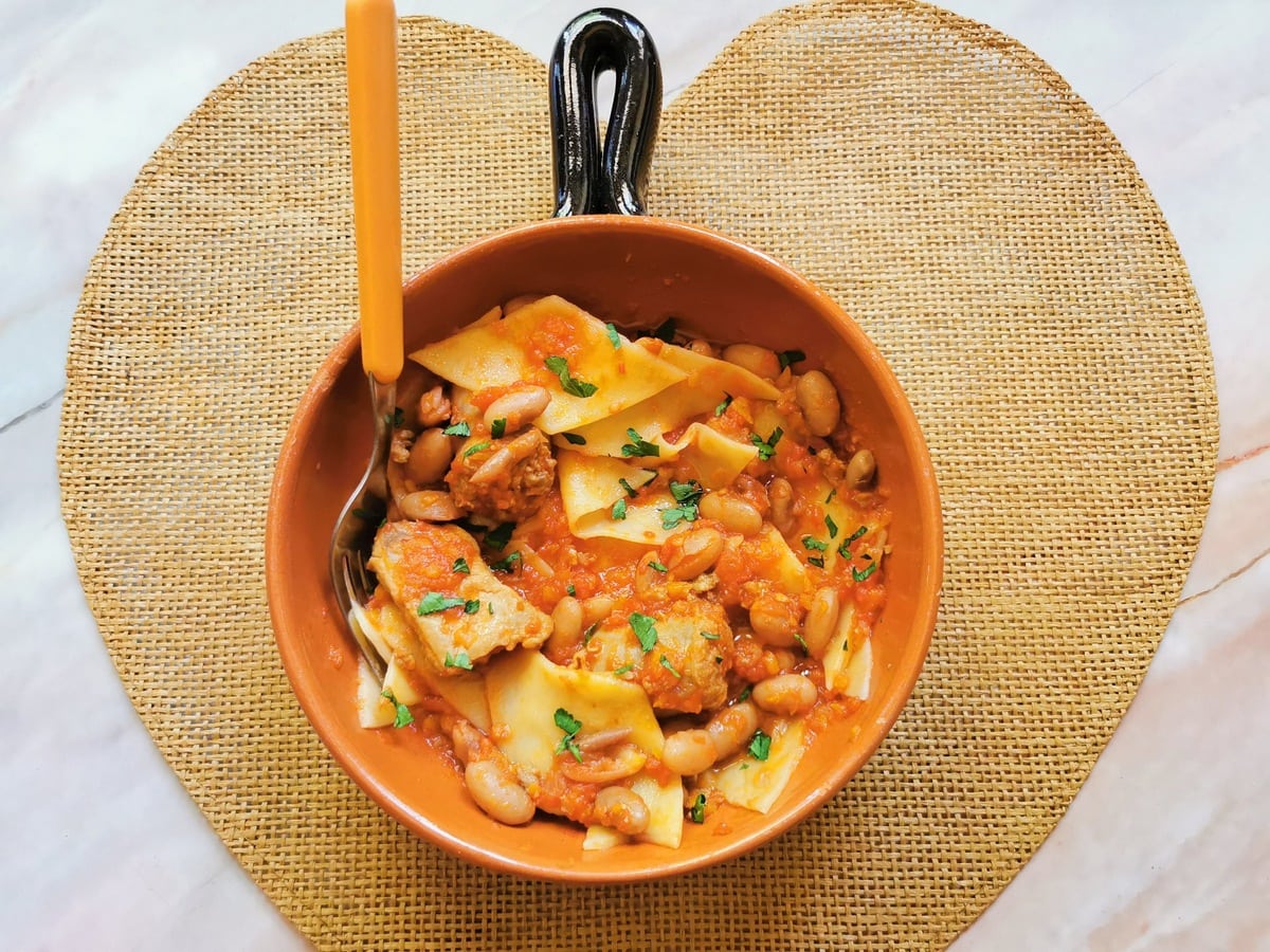 A serving of homemade maltagliati sausage pasta in a round terracotta bowl with a fork.