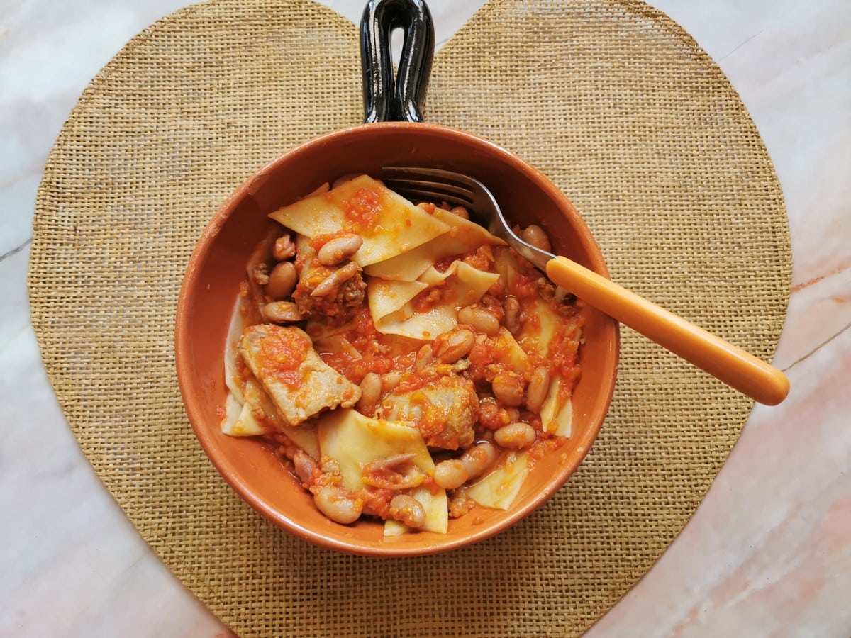 homemade malatagliati with sausage and bean sauce in terracotta bowl.