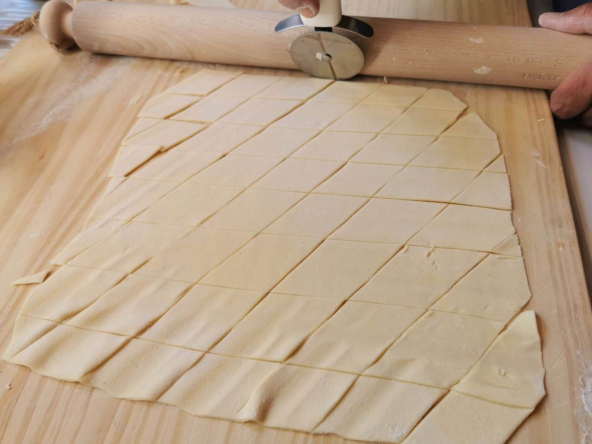 Maltagliati dough sheet cut into diamons (rhombuses) on a wooden pastry board.