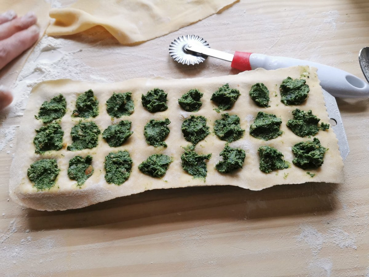 Dough sheet on ravioli mold with filling in each depression.