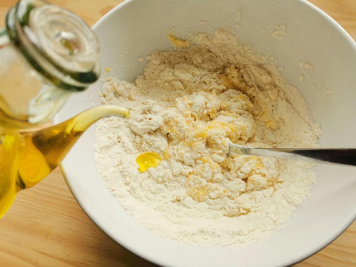 Flour and eggs mixed together in white bowl and olive oil being poured in.