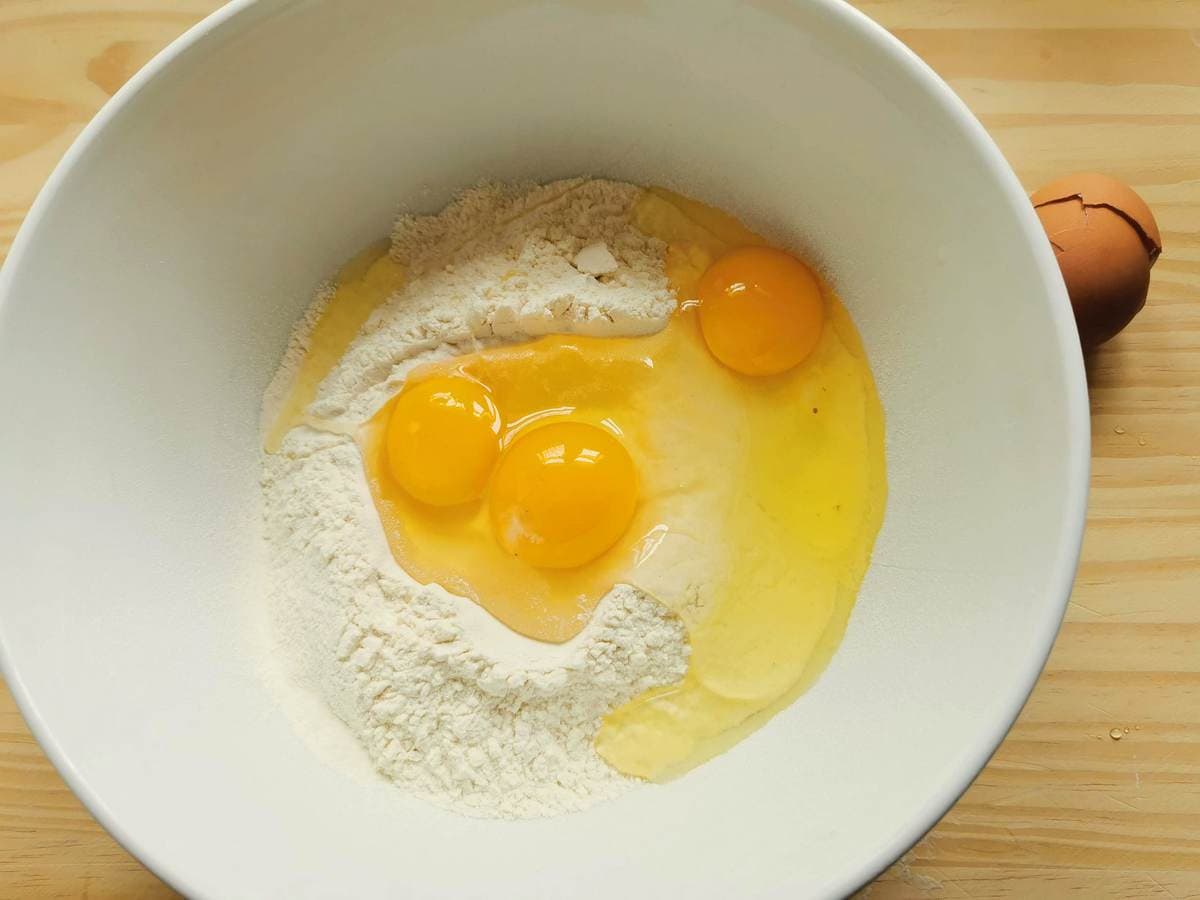 Soft wheat flour and 3 raw eggs in a white bowl.