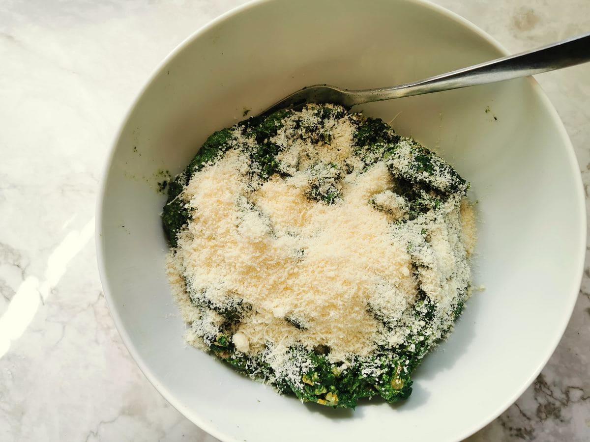 Ravioli filling in white bowl with grated parmigiano cheese on top.