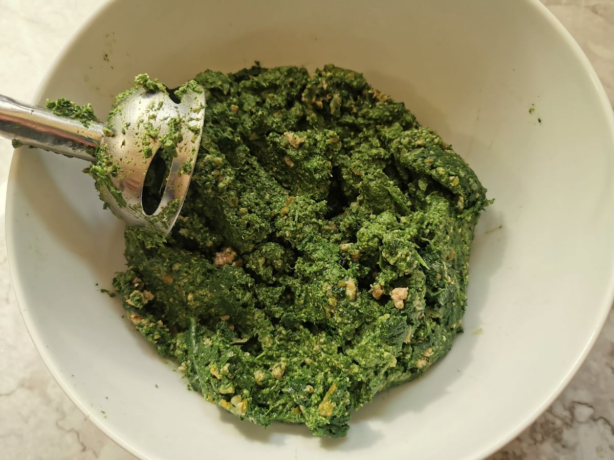 Puréed ravioli filling in white bowl with immersion blender.