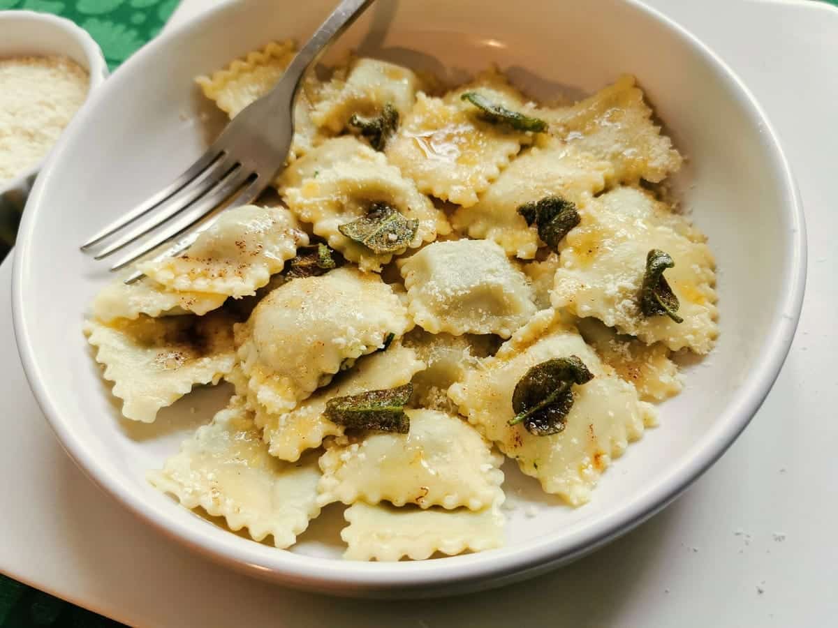 Homemade meat ravioli (agnolotti) served with melted butter and crispy sage in white bowl.