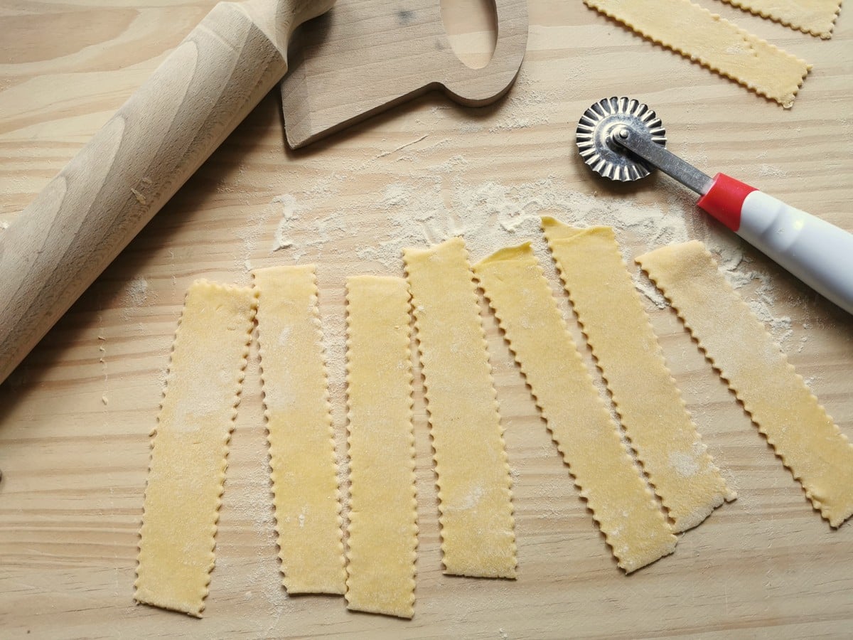 Homemade egg pasta ribbons on flour dusted wood work top.