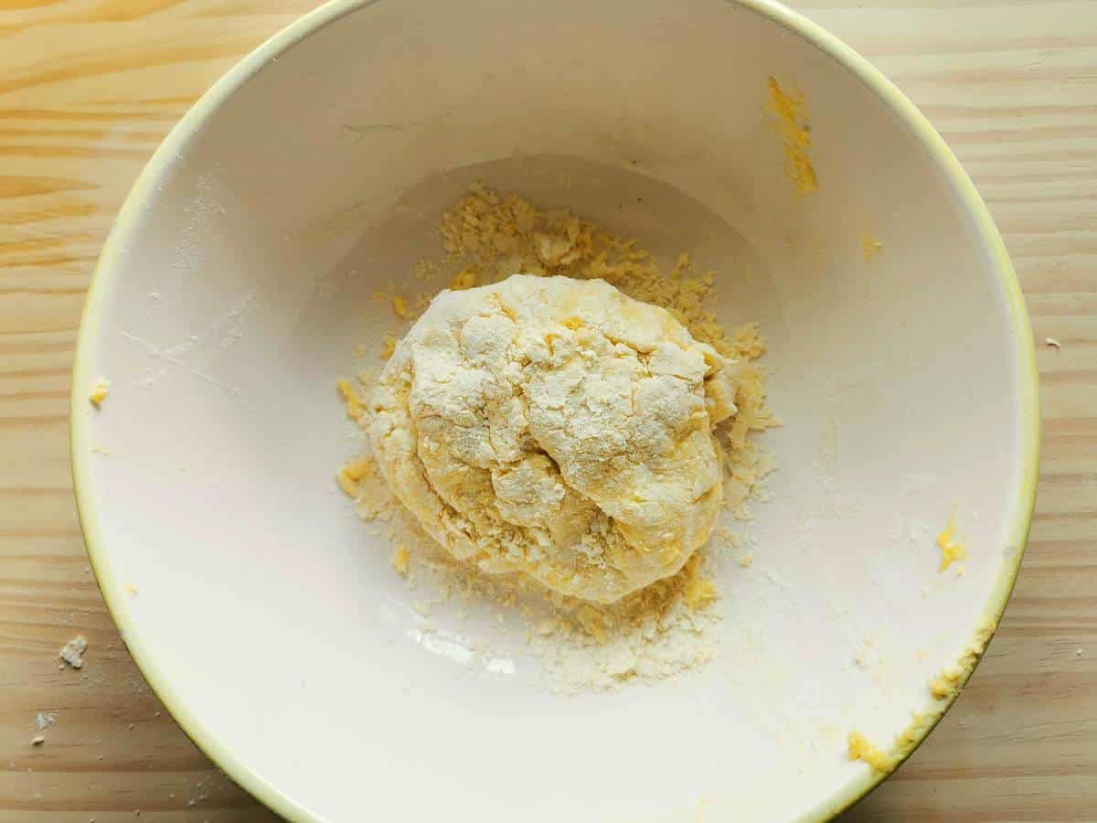 A ball of egg pasta dough in white bowl.