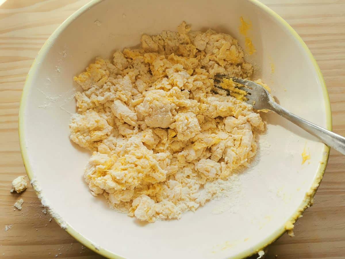 Flour and eggs mixed together with a fork in white bowl.
