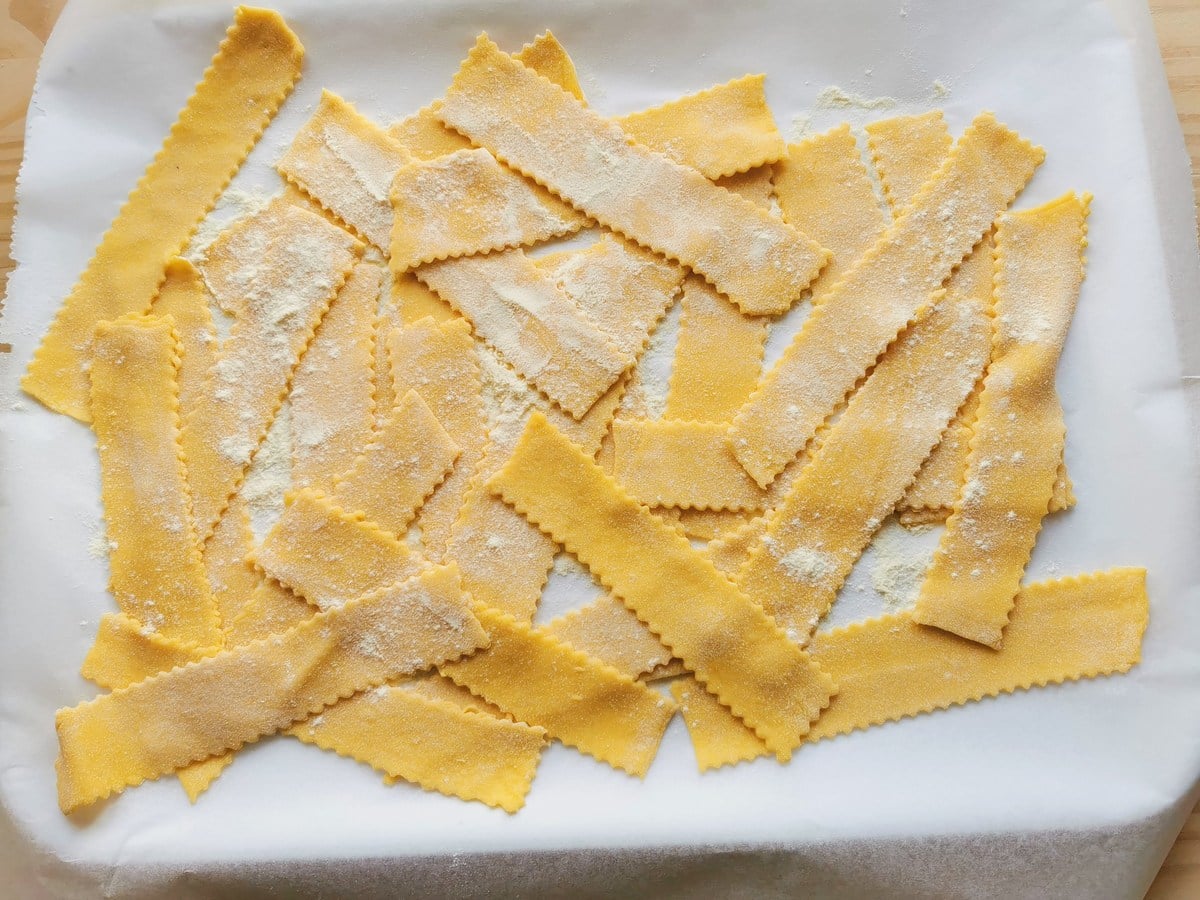 Homemade pasta ribbons on white tray dusted with semolina flour.