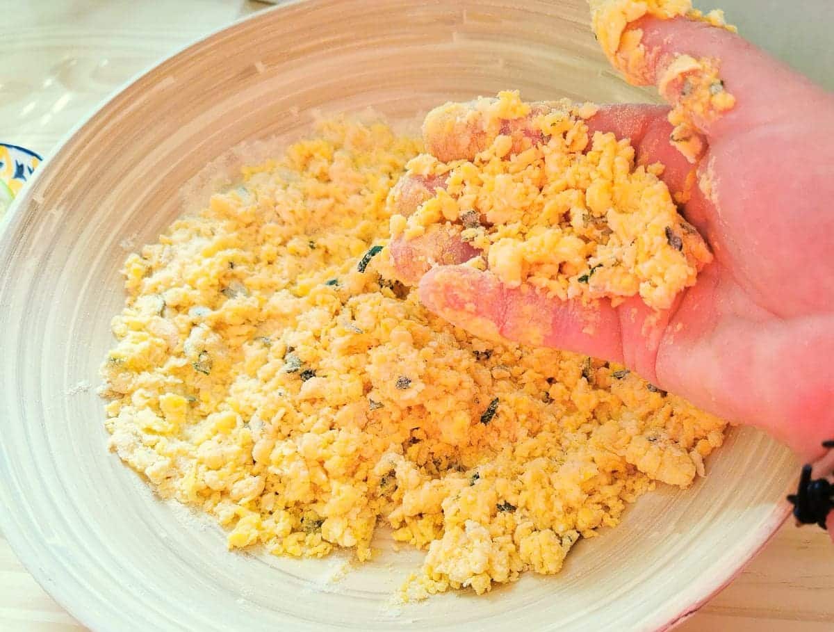 Pasta dough being crumbled in large bowl.