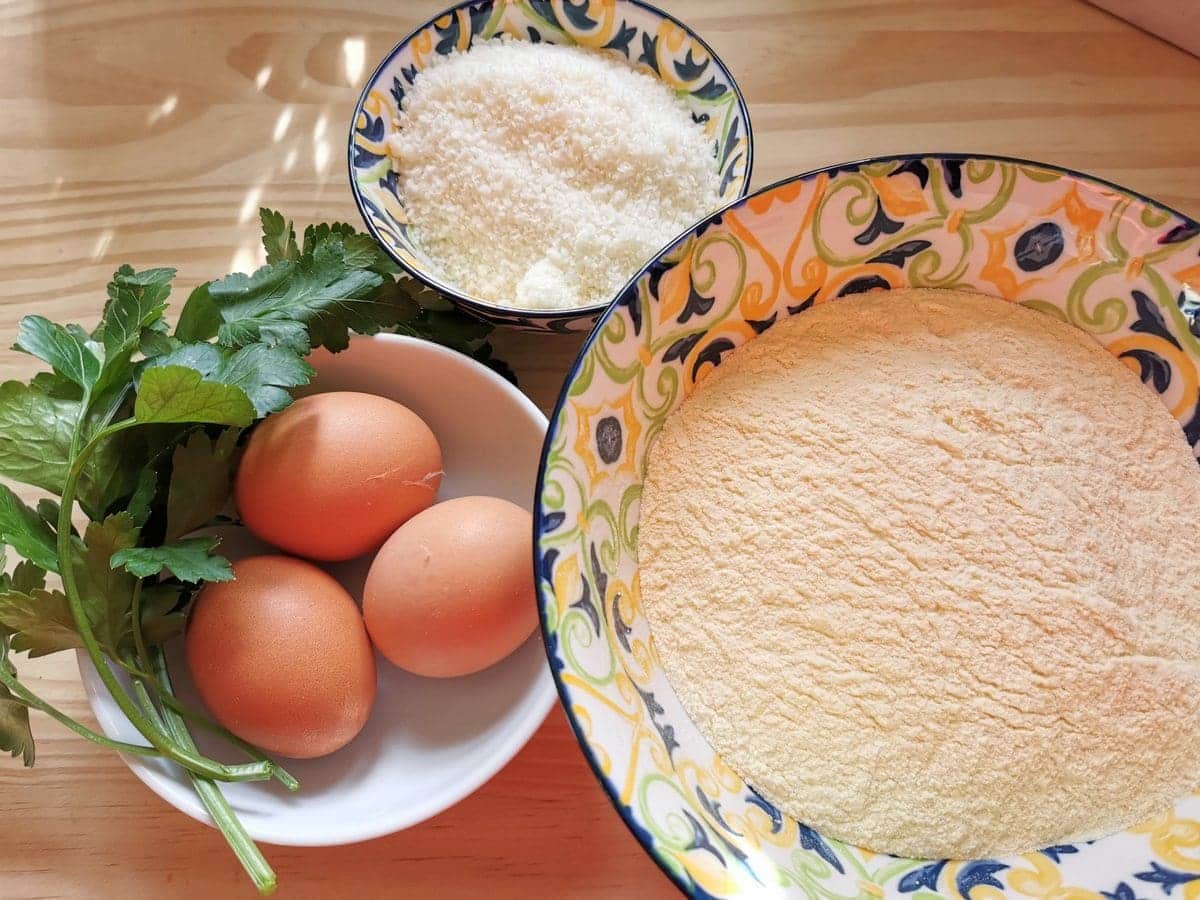 Ingredients for homemade pastina (millefanti), eggs, parsley, semolina flour and grated Parmigiano in separate bowls.