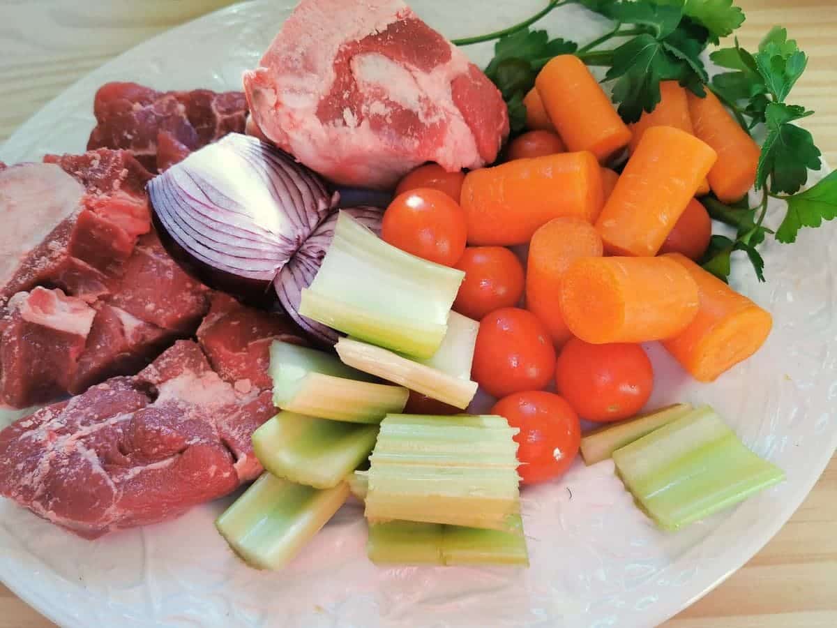 Prepared ingredients for beef broth on oval white plate.