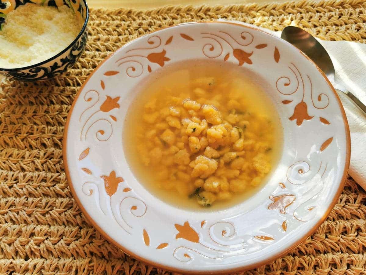 Homemade cheese, egg and parsley pastina in broth in white bowl.