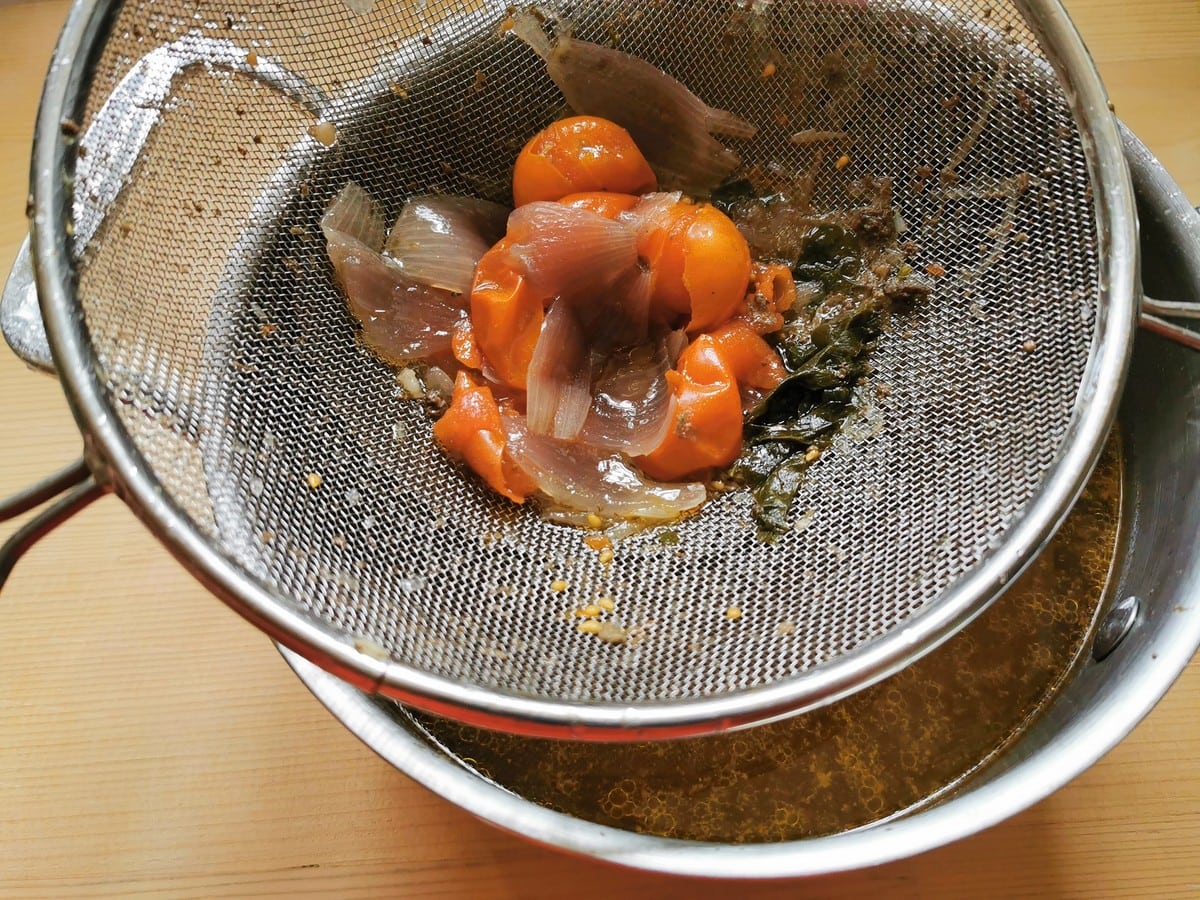 Beef broth being filtered through a fine sieve which has cooked vegetables in it.