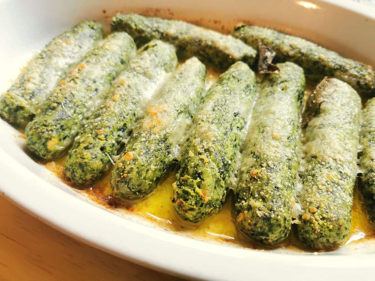 Baked spinach ricotta gnocchi in white oval oven dish.