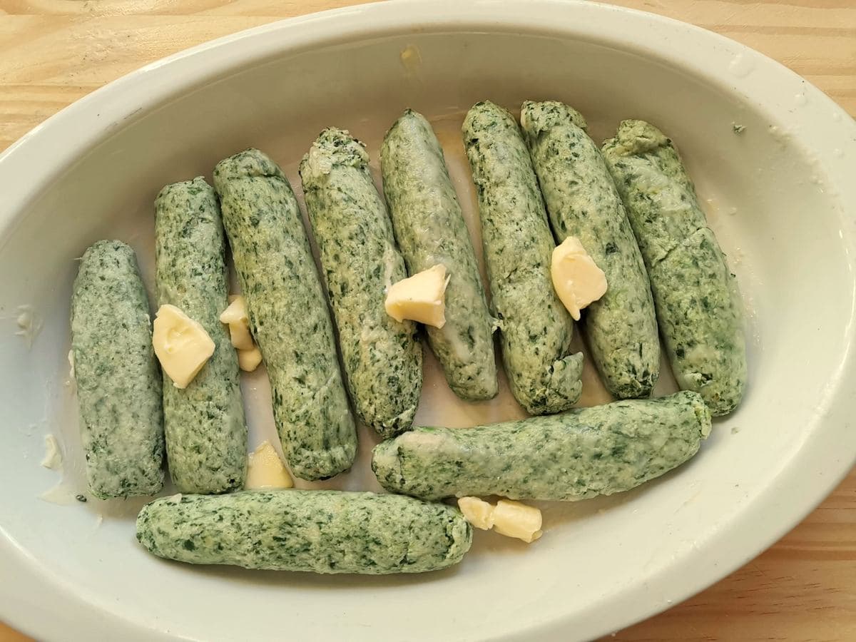 Boiled spinach ricotta gnocchi in oval oven dish with pieces of butter.