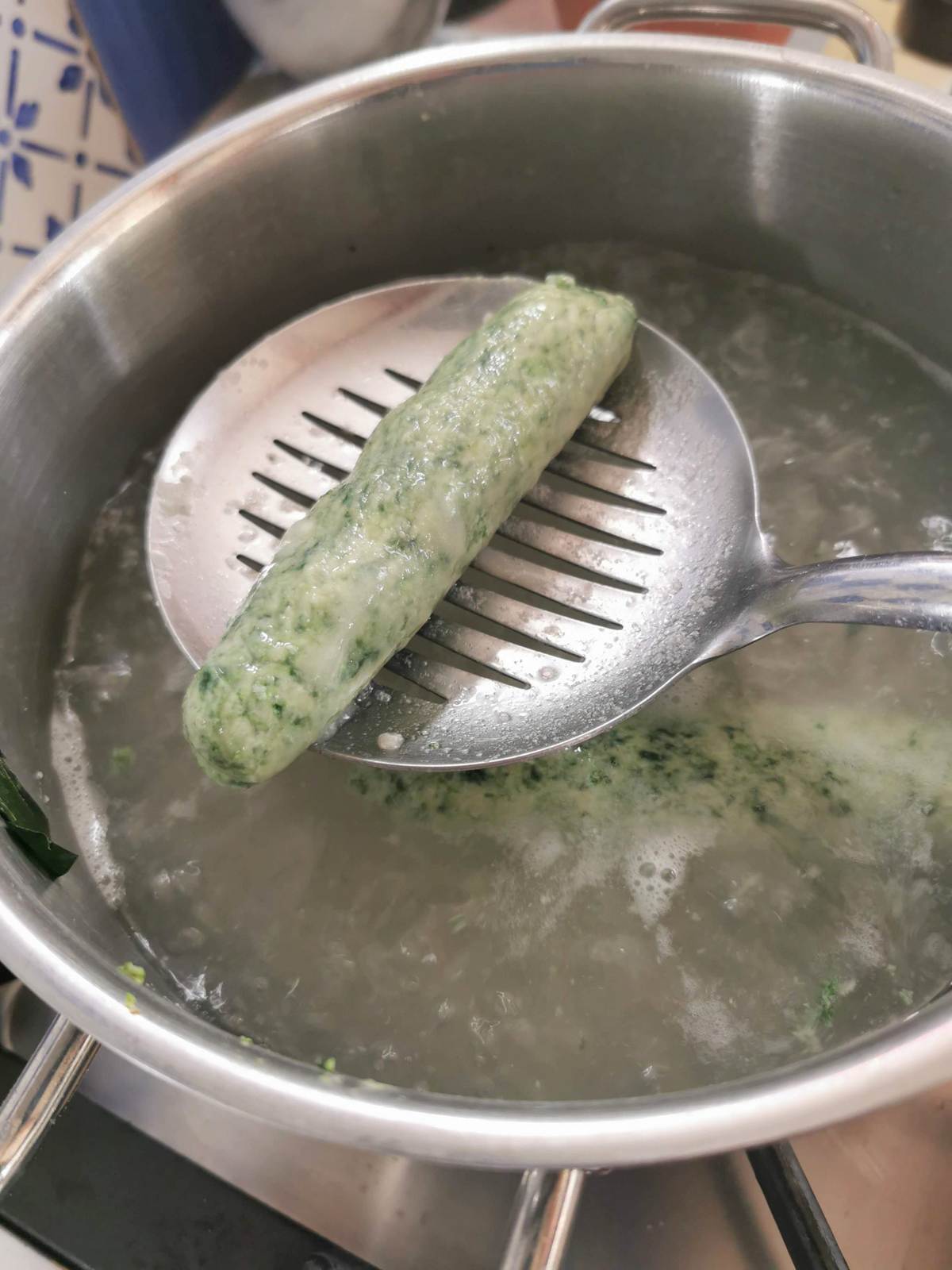One spinach gnocchi on slotted spoon held over pot of boiling water.