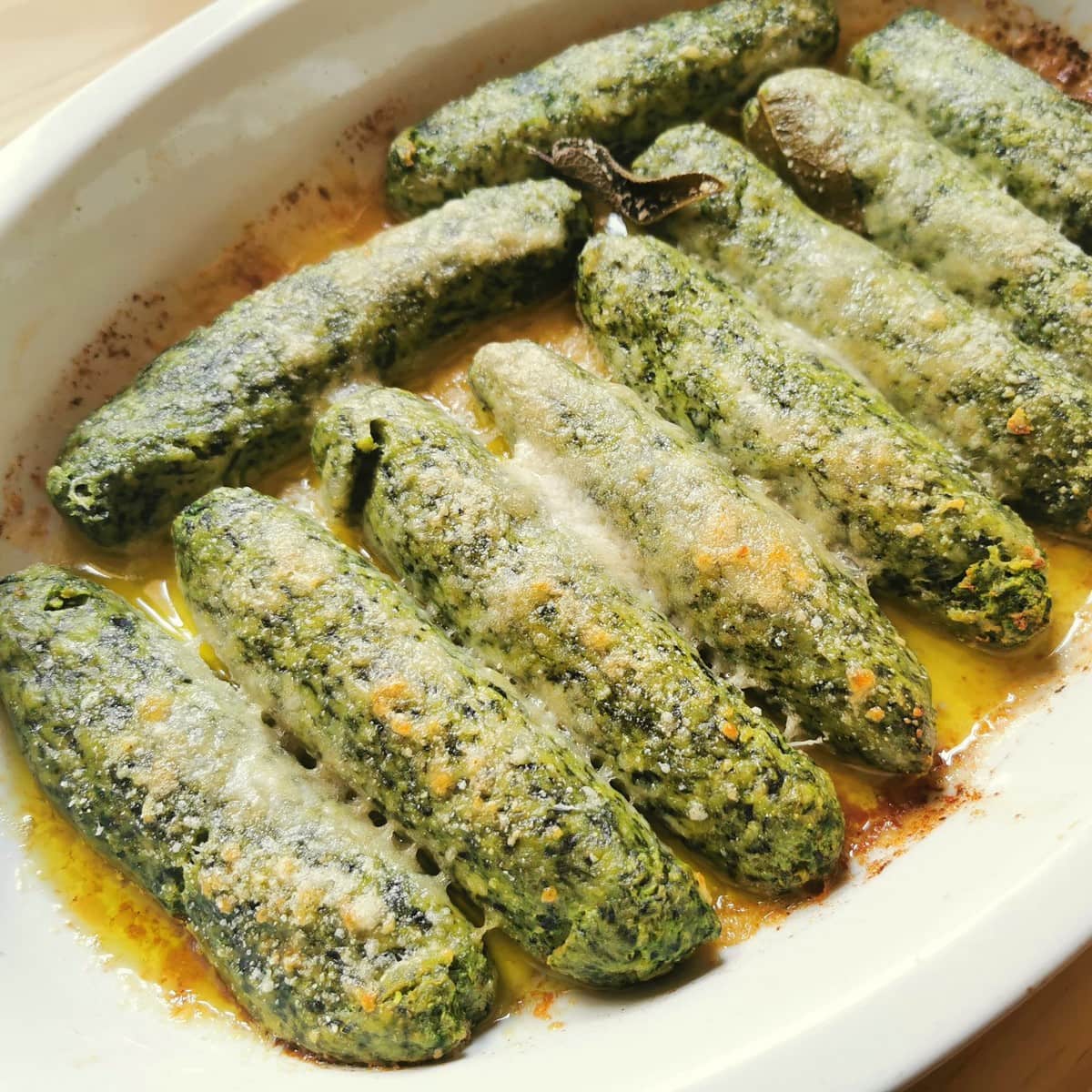 Large baked spinach ricotta gnocchi in white oval oven dish.