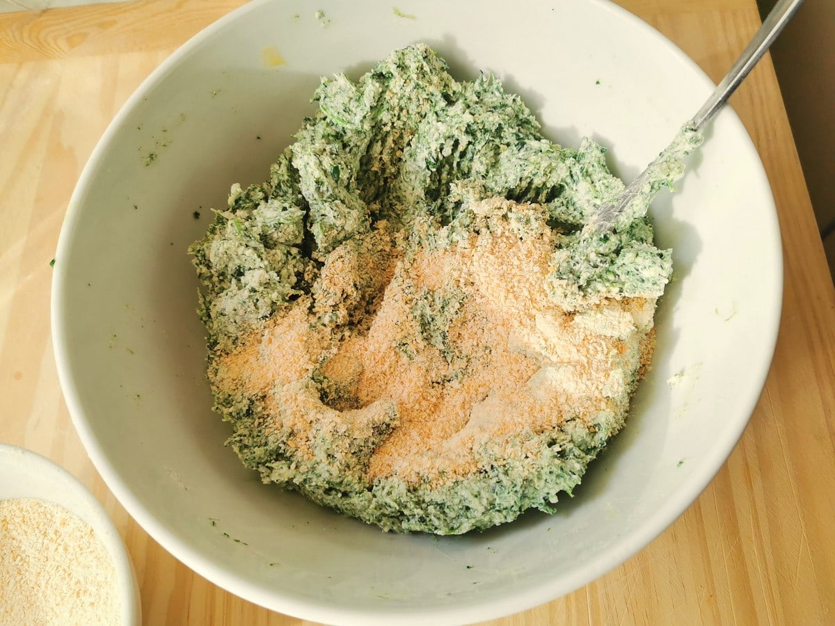 Breadcrumbs added to white bowl with spinach and ricotta gnocchi mixture.