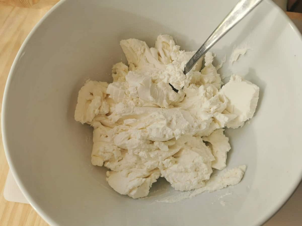 Mashed fresh ricotta in a white bowl with fork.