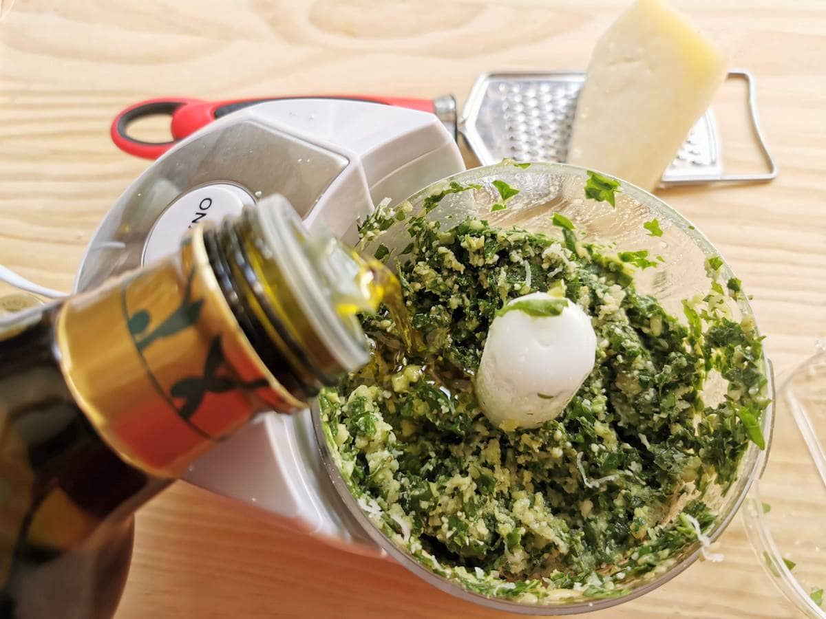 Olive oil being added to basil pesto in food processor